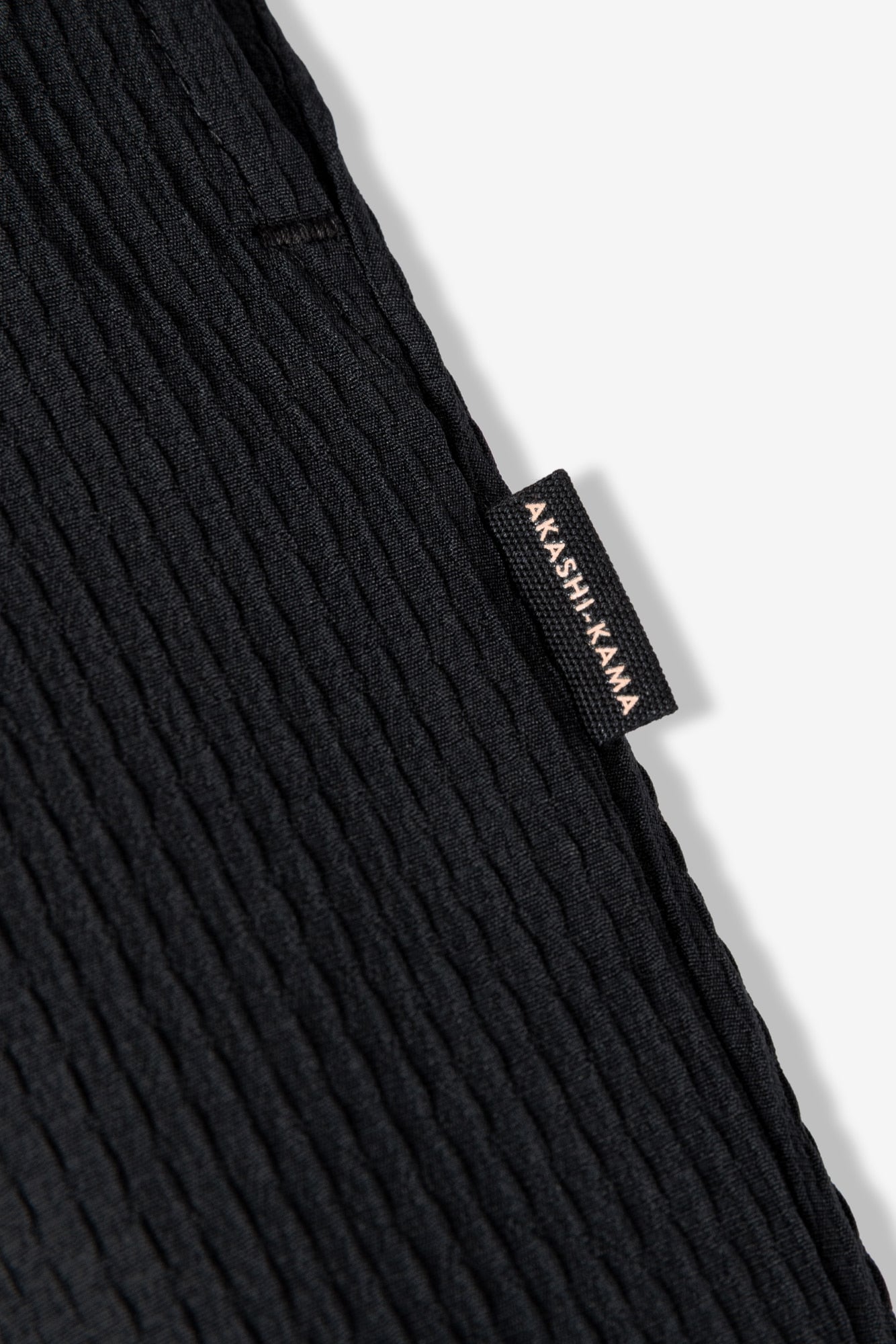 AKASHI-KAMA side label on black textured Sashiori pleated tailored pants